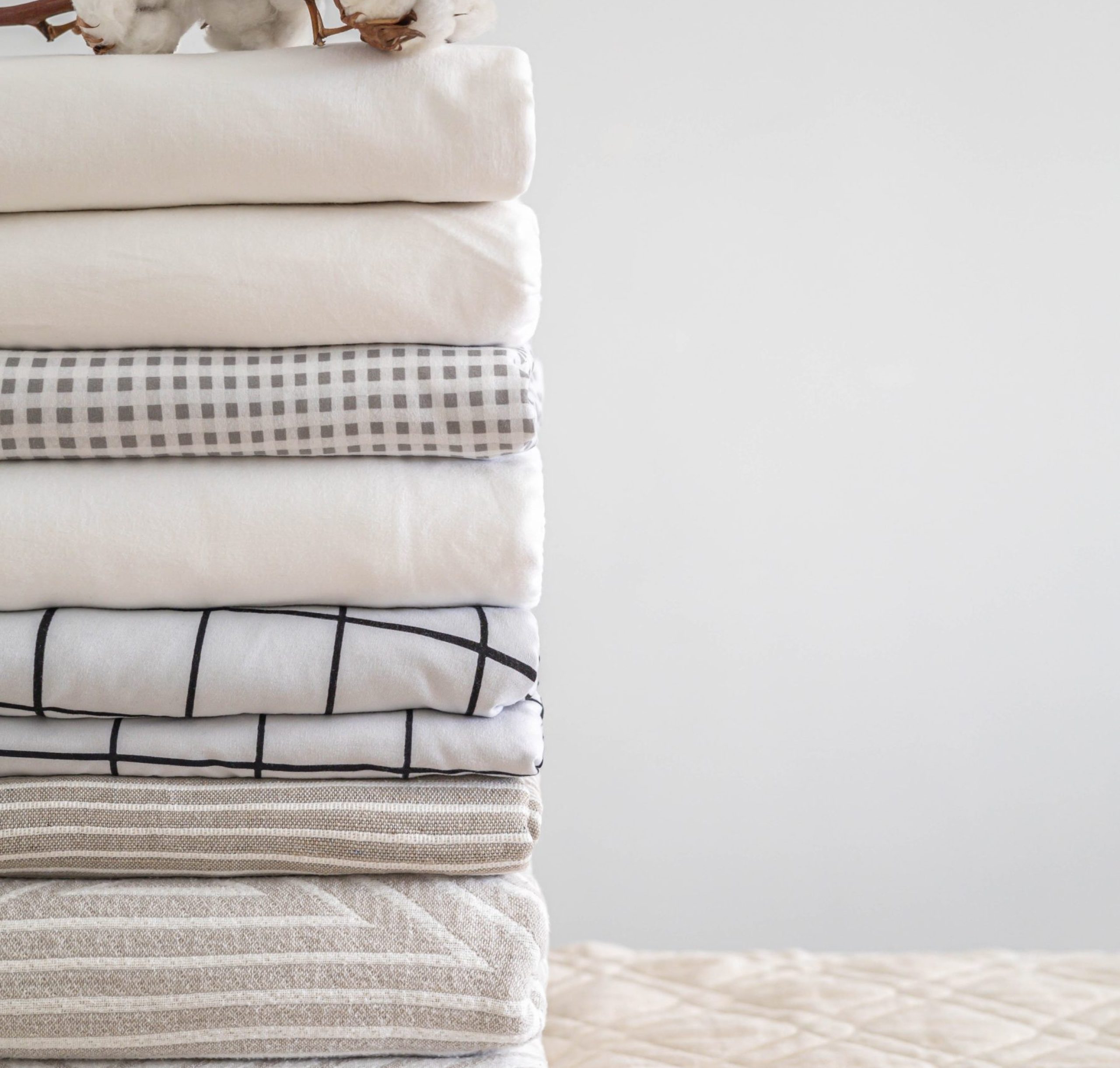 Cotton branch with pile of neatly folded bed sheets, blankets and towels. Production of natural textile fibers. Manufacture. Organic product.